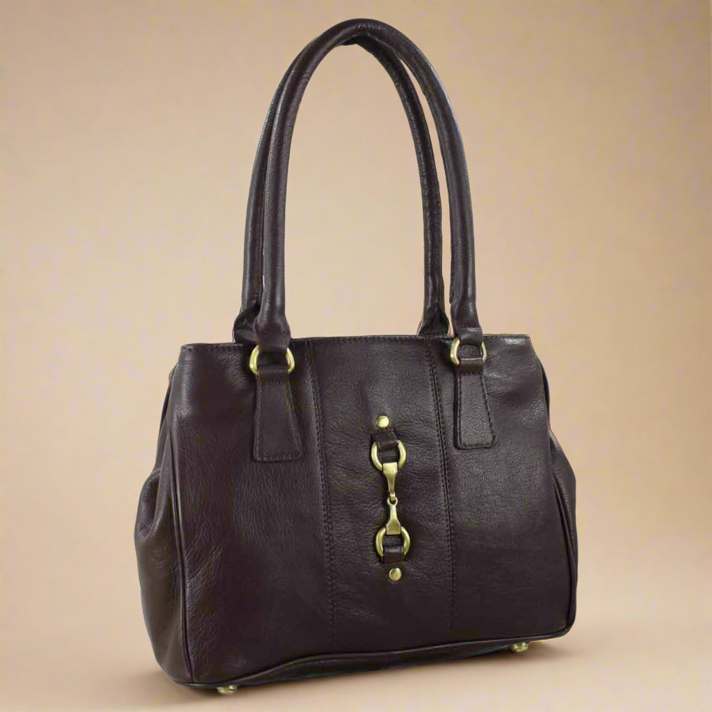 Dark brown leather handbag with gold/brass hardware on a beige background with snaffle bit horse bit fitments. equestrian. country.