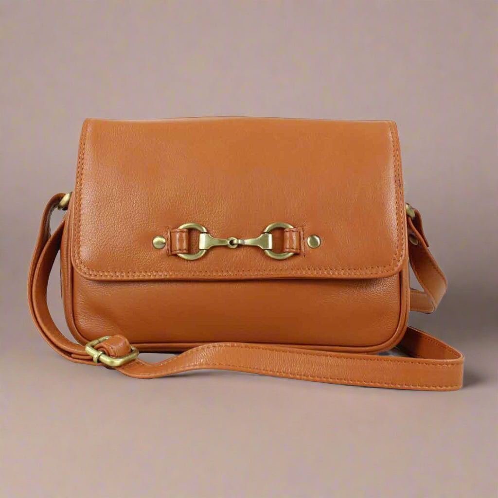 A tan leather handbag with a metal bit fastener on the front and a shoulder strap.