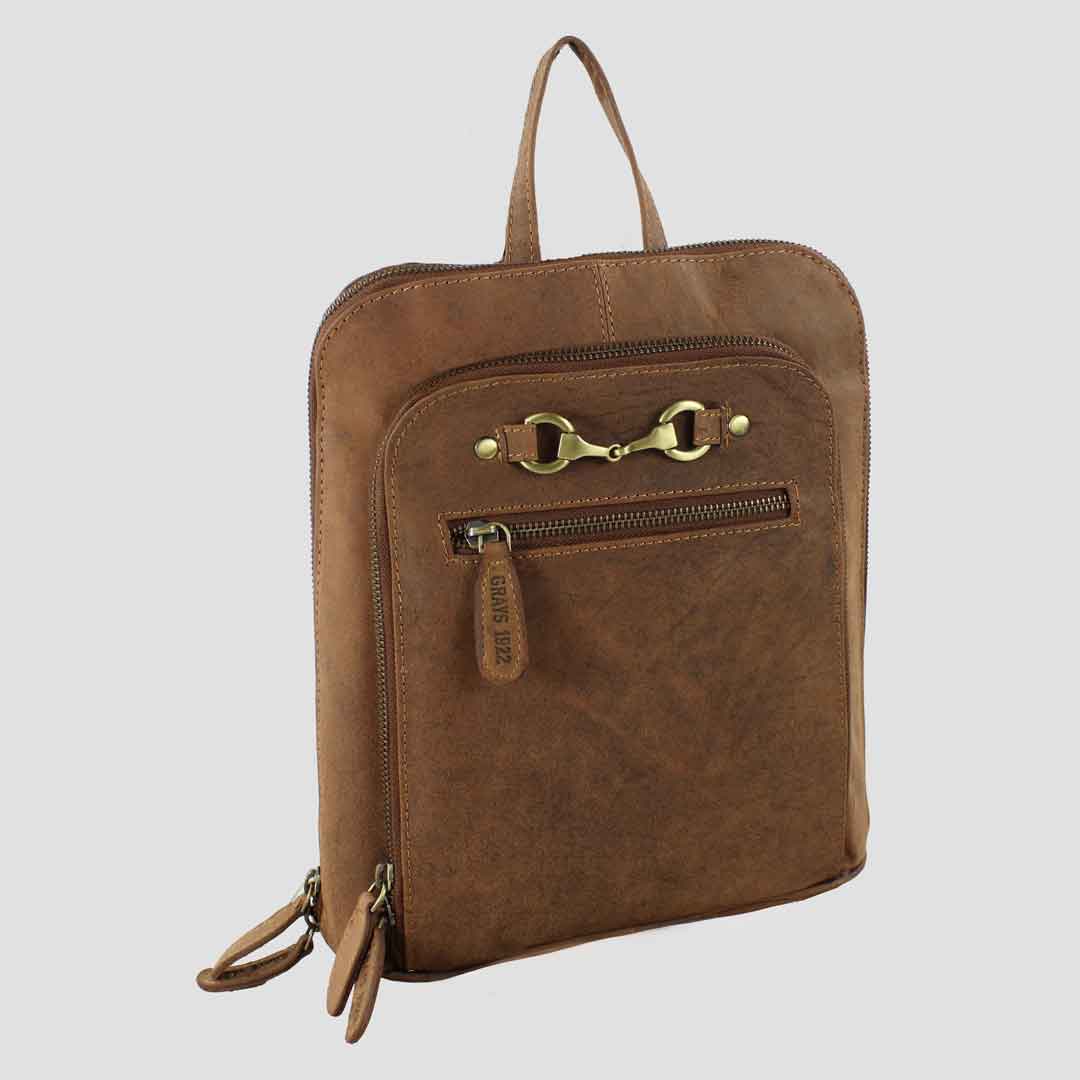 Brown leather backpack with gold zipper and a snaffle bit fitment on a light gray background. insipred by country and equestrian