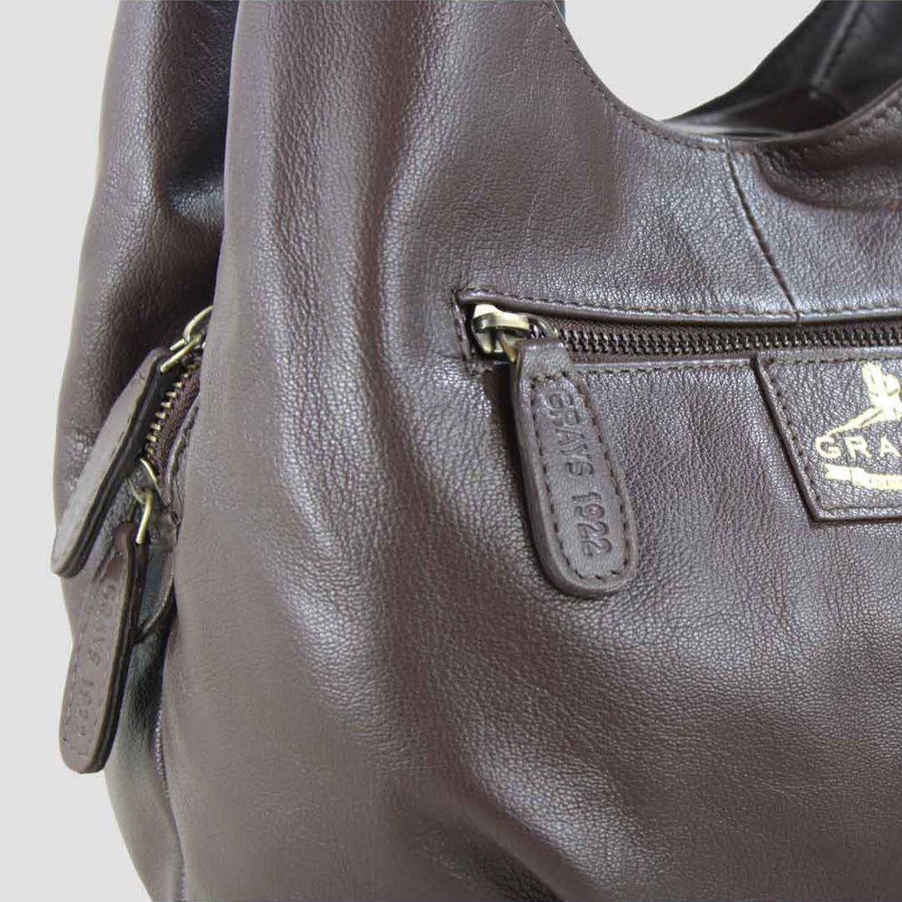 Close-up of a brown leather handbag with a visible brand logo on a light gray background